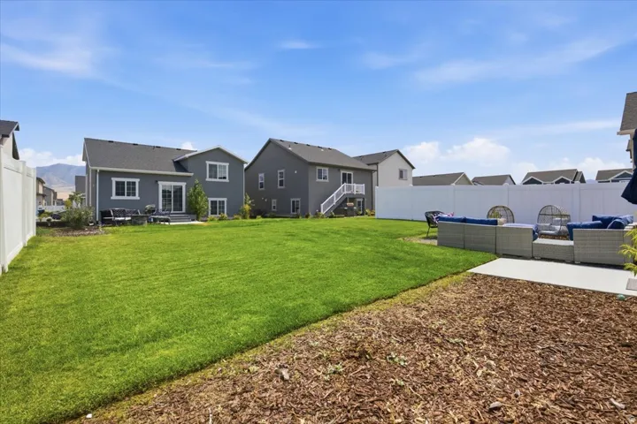 Expansive backyard featuring a manicured lawn, white privacy fencing, and a concrete patio