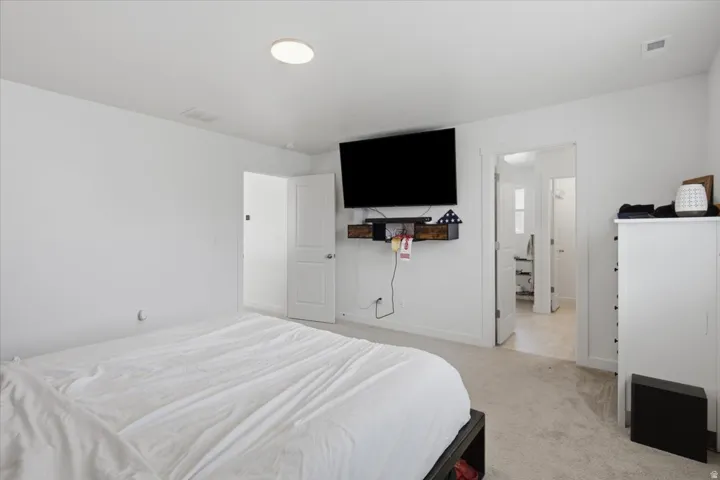 Maste bedroom featuring recessed ceiling lighting, wall-mounted television, wood-finish floating shelf, white paneled doors, and carpeted flooring
