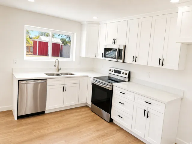 White shaker cabinetry, stainless steel appliances, light-toned wood-finish flooring, undermount sink, and light countertops
