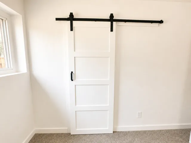 White paneled barn door with black hardware, complementing light neutral wall finishes and carpeted flooring