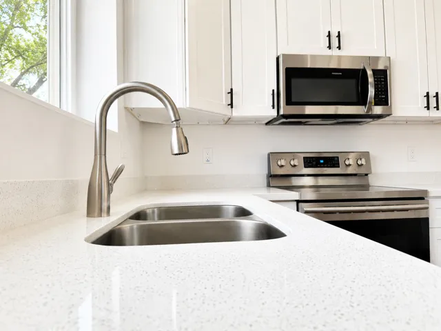 White cabinetry with black hardware, stainless steel appliances, dual basin sink with gooseneck faucet, and light-toned countertops