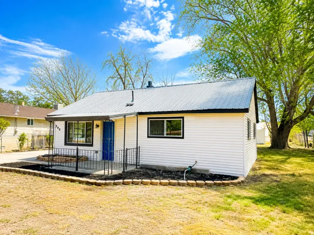 White horizontal siding exterior, metal roof, black trim windows, covered porch with metal railing, and a vibrant blue entry door