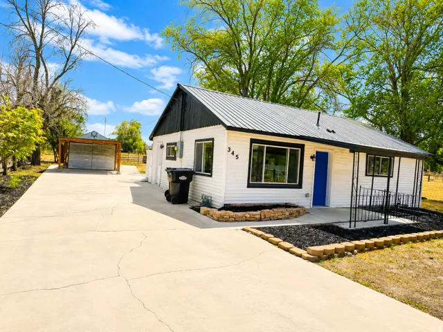 White siding exterior with a metal roof, contrasting black trim, and a vibrant blue entry door