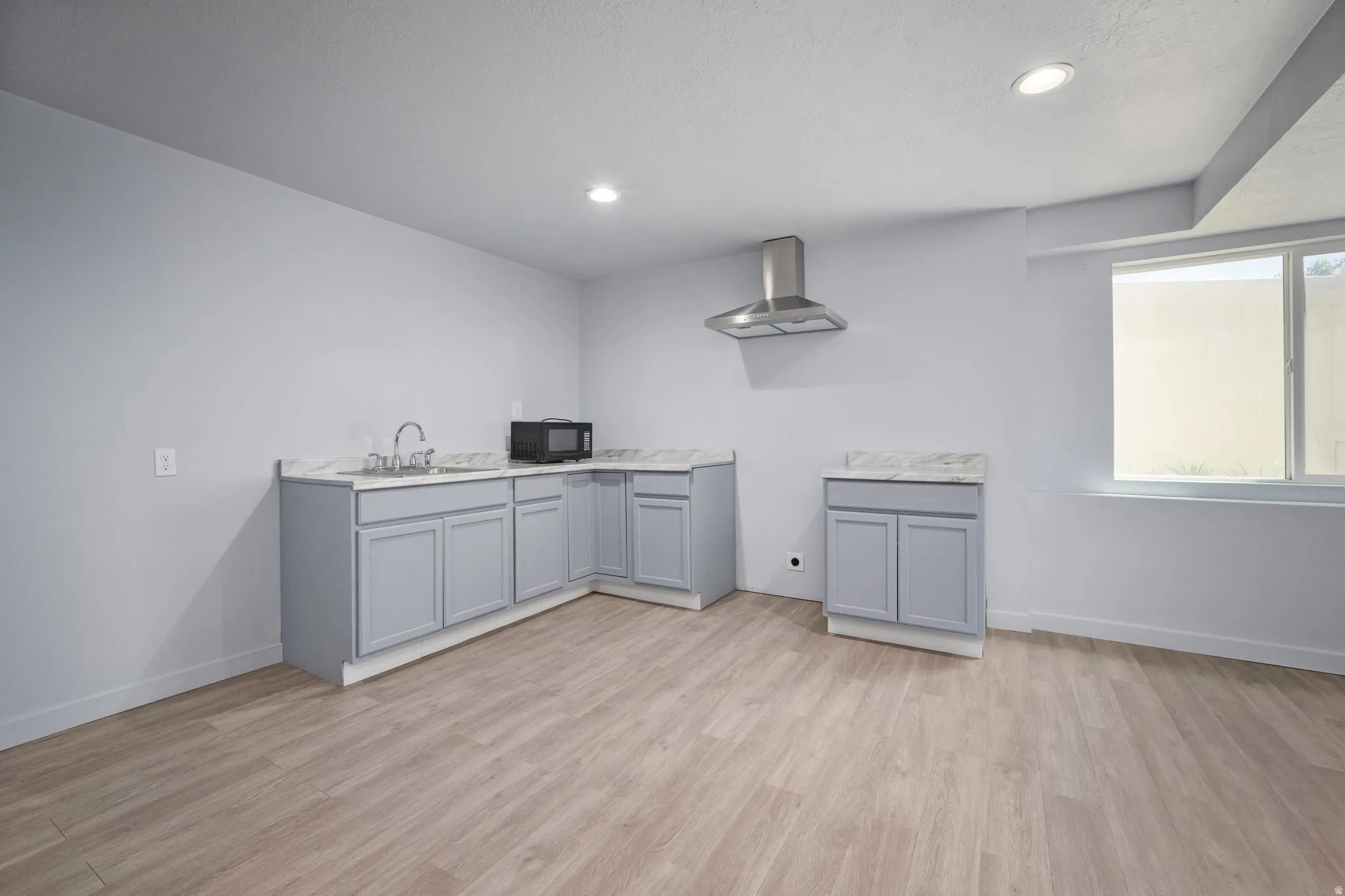 Wood-finish flooring with light gray cabinetry, white countertops, stainless steel range hood, and recessed lighting