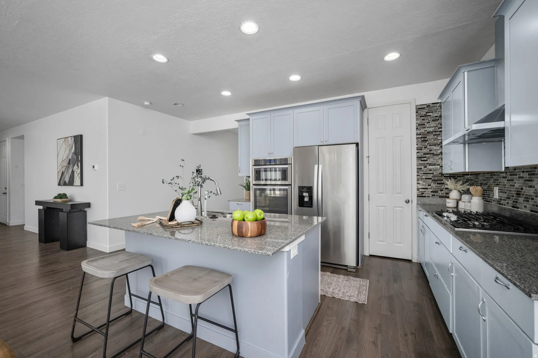 Kitchen featuring light blue cabinetry, stainless steel appliances, a granite island with an undermount sink, and wood-finish flooring