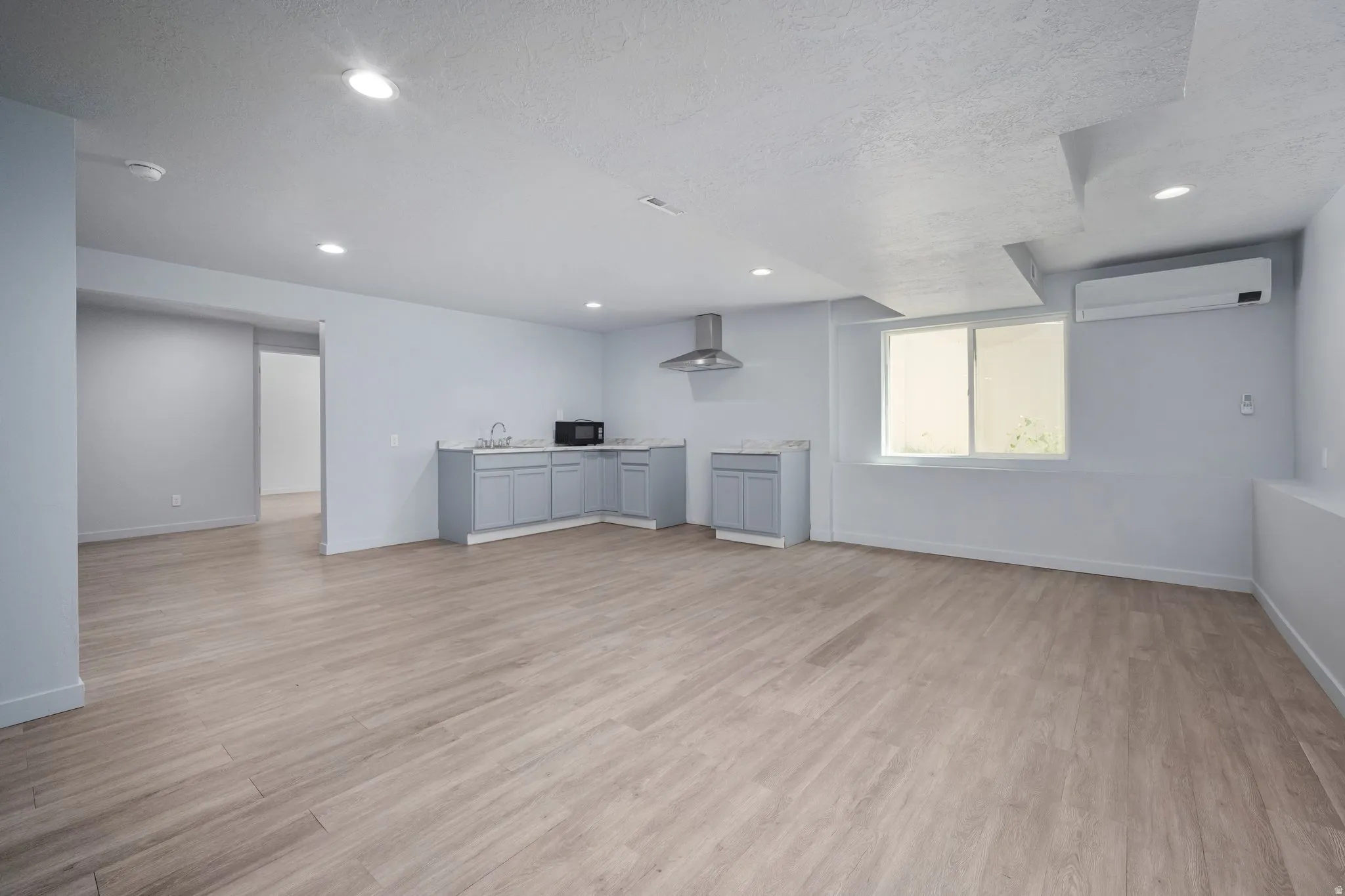 Open concept living area featuring wood-finish flooring, recessed lighting, and a built-in kitchenette with light gray cabinetry and a stainless steel range hood
