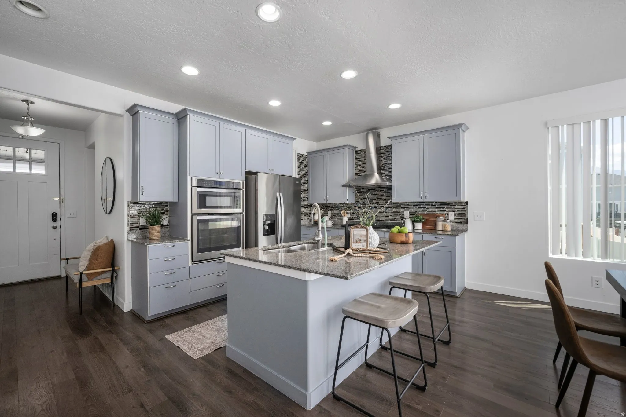 Kitchen featuring an island with a built-in sink, stainless steel appliances, light gray cabinetry, and a textured backsplash