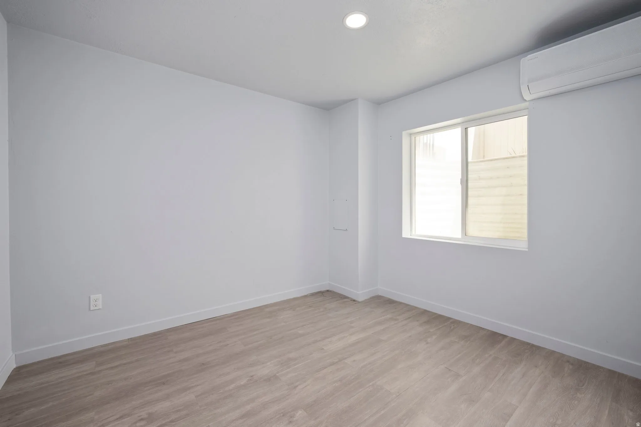Recessed ceiling lighting, wood-finish flooring, white walls, window, and wall-mounted air conditioning unit