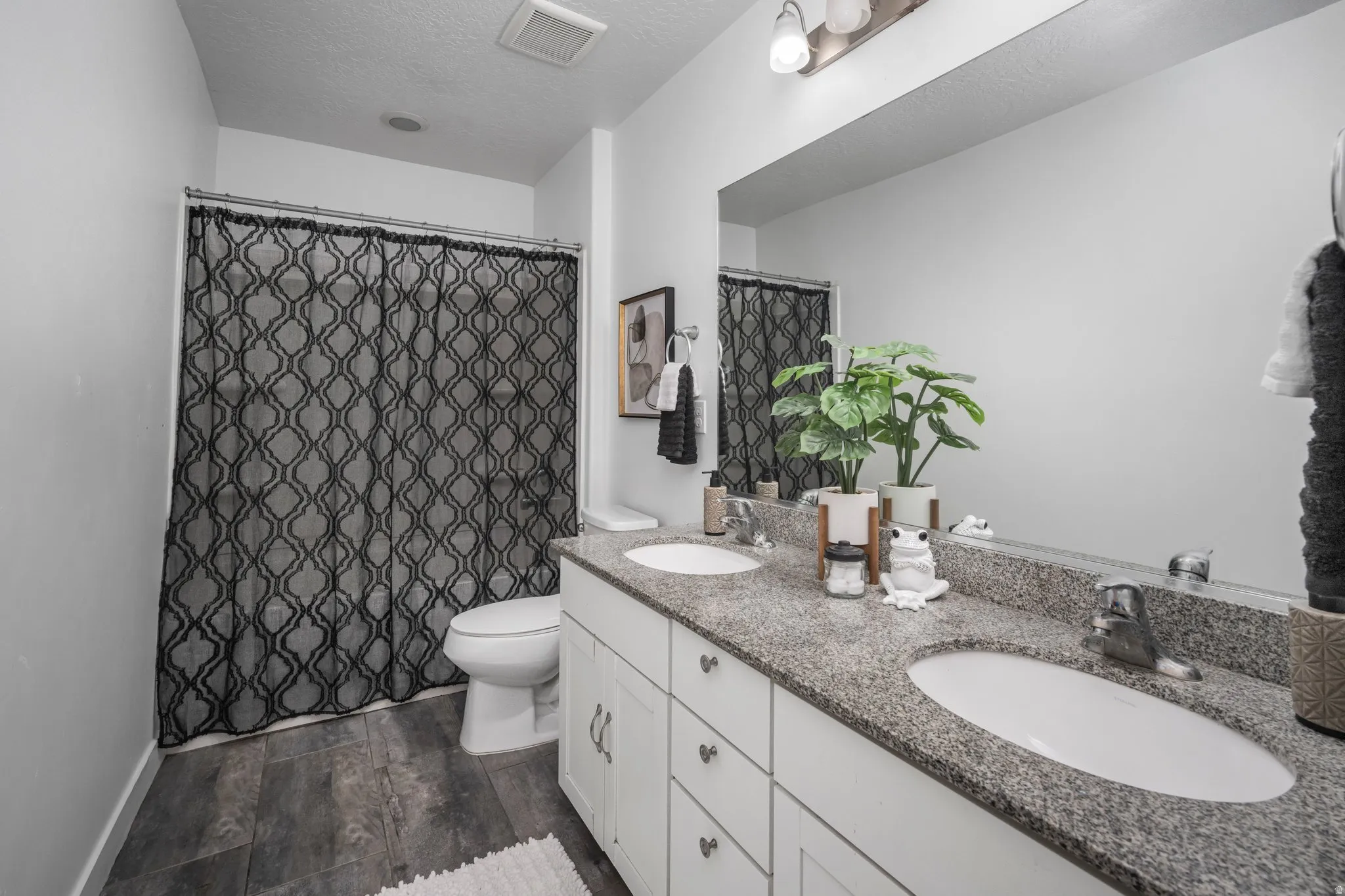 Dual vanity with a speckled countertop, white cabinetry, and wood-finish flooring