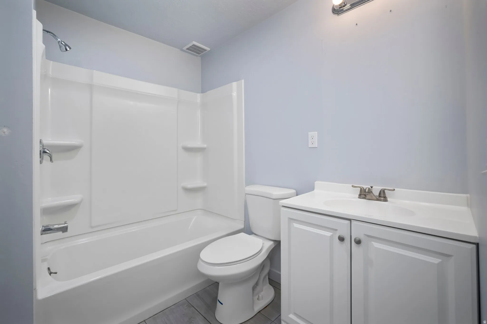 White tub with shower surround, white vanity with integrated sink, and brushed nickel fixtures