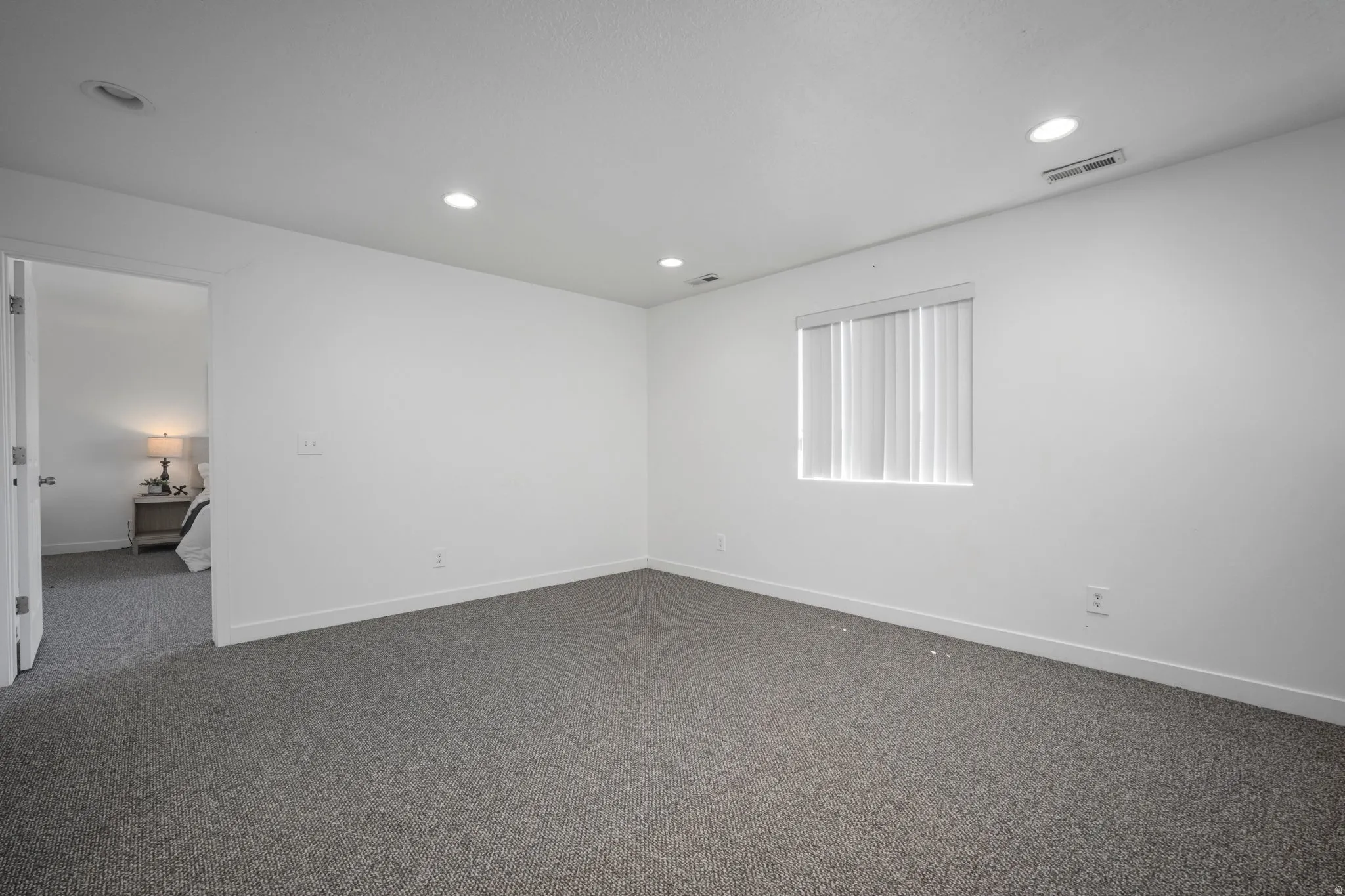 Neutral gray carpeting, white painted walls, recessed ceiling lighting, and a window with blinds