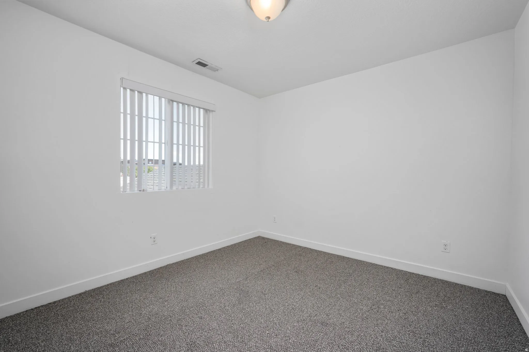 Textured carpeting, neutral wall finishes, window with vertical blinds, and a flush mount ceiling light fixture