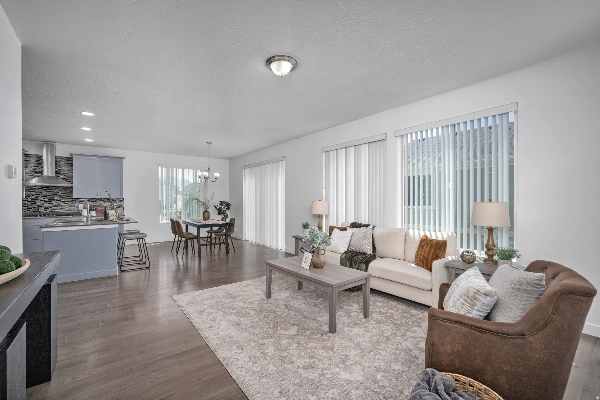 Open-concept living space featuring wood-finish flooring, recessed lighting, and large windows with vertical blinds