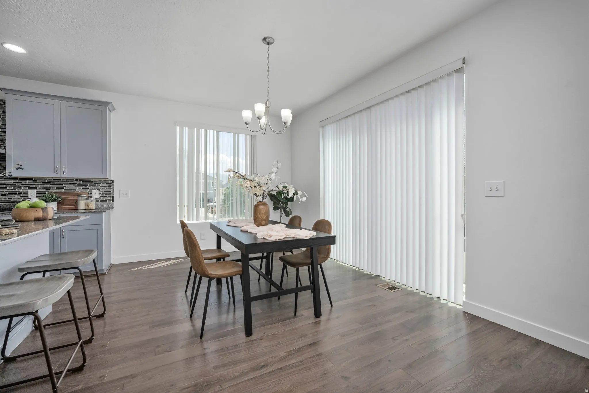 Open-concept dining area with wood-finish flooring, a contemporary chandelier, and a sliding glass door with vertical blinds