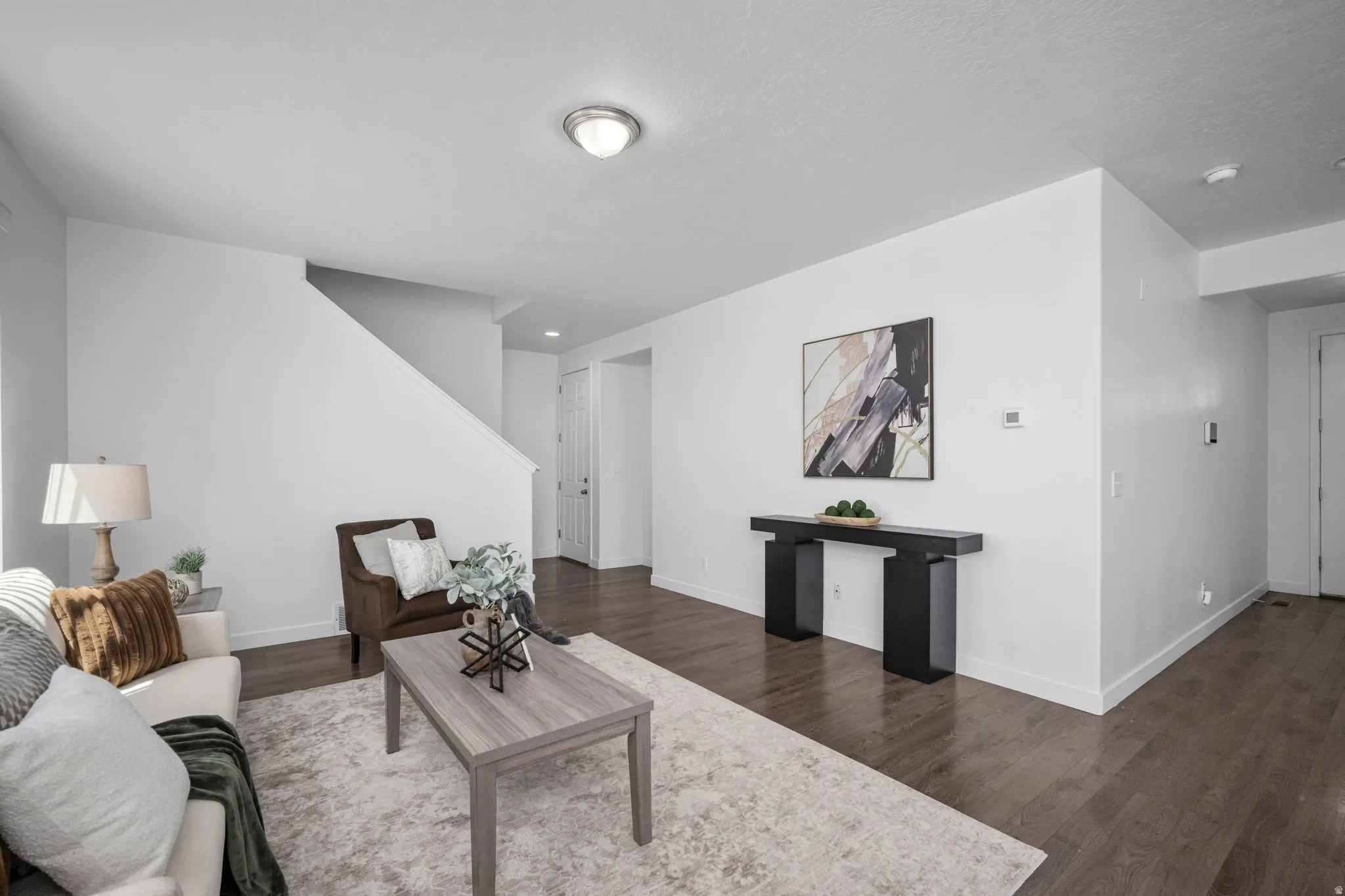 Open-concept living space with wood-finish flooring, white walls, and a staircase with a white railing