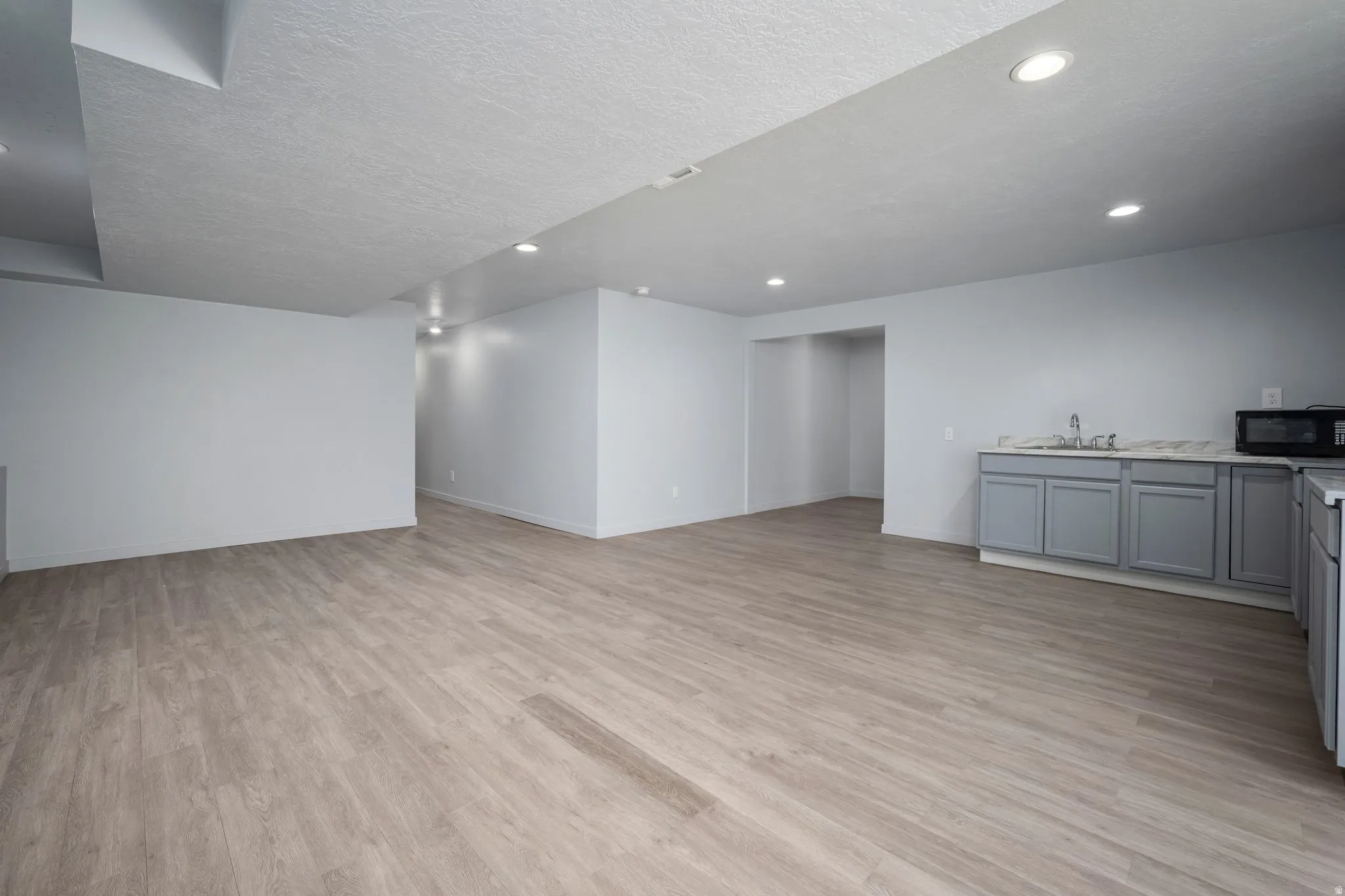 Spacious room featuring wood-finish flooring, recessed lighting, and a built-in wet bar with gray cabinetry, a sink, and a light-toned countertop