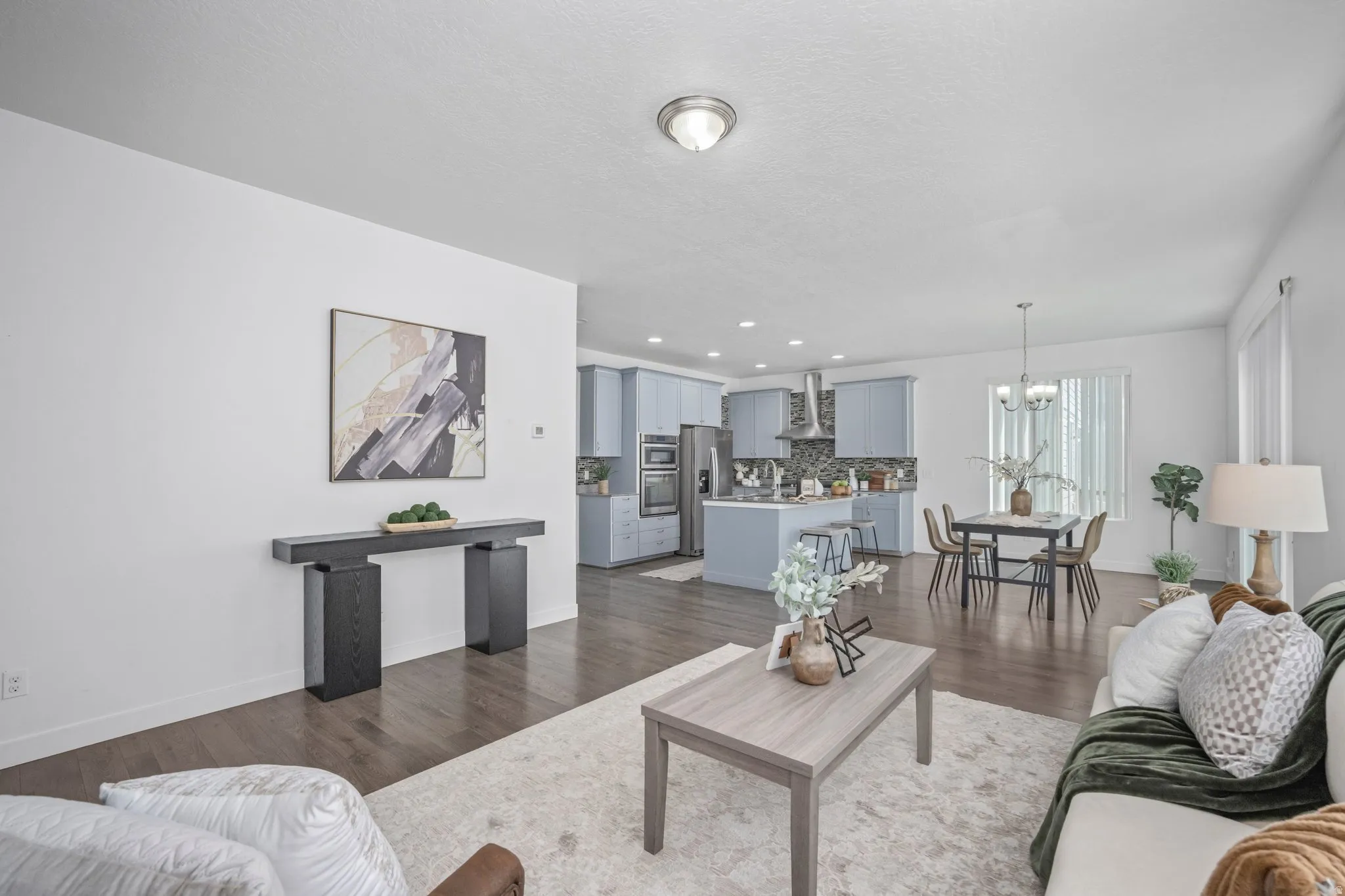 Open-concept living space featuring wood-finish flooring, a modern kitchen with light blue cabinetry, stainless steel appliances, and a dining area with chandelier lighting