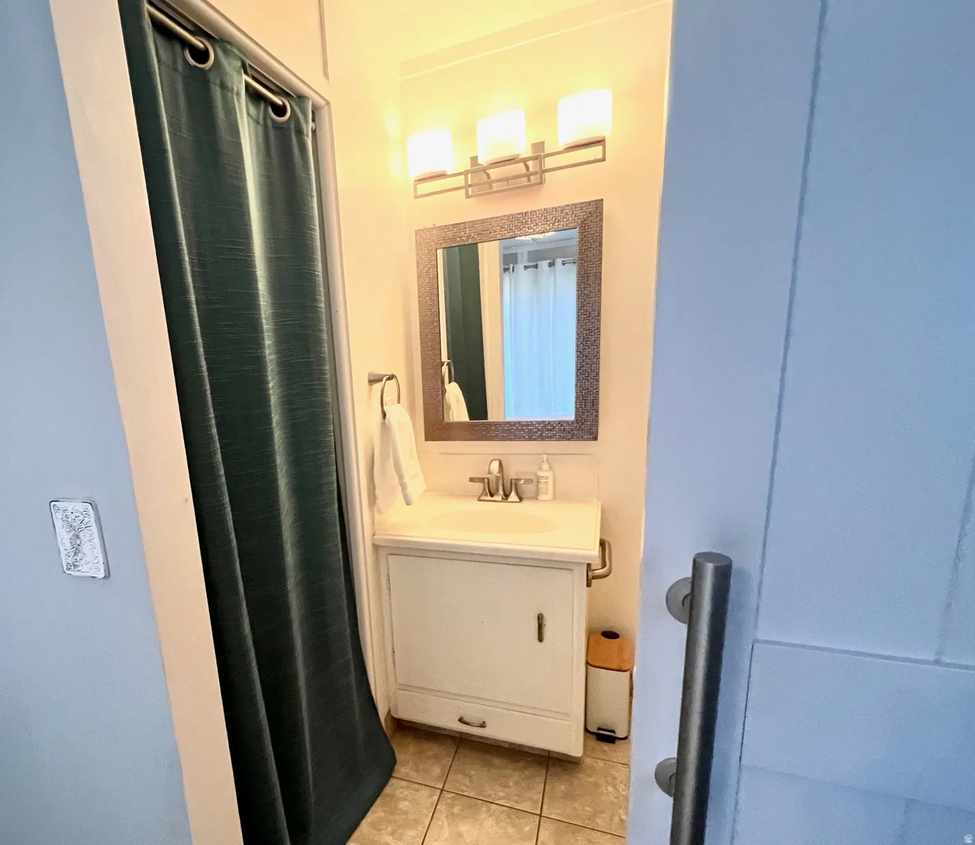 Vanity with integrated sink, framed mirror, wall-mounted light fixture, and tile flooring