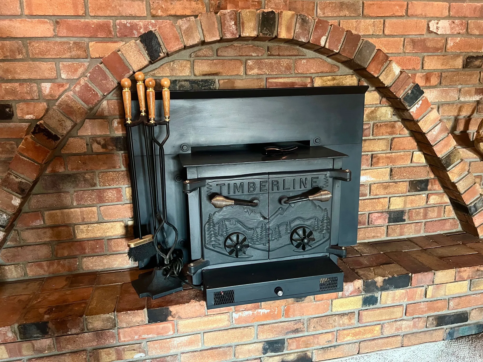 Charming brick fireplace featuring a traditional arched opening, cast iron insert stove with decorative detailing, and wrought iron fireplace tools including poker and tongs