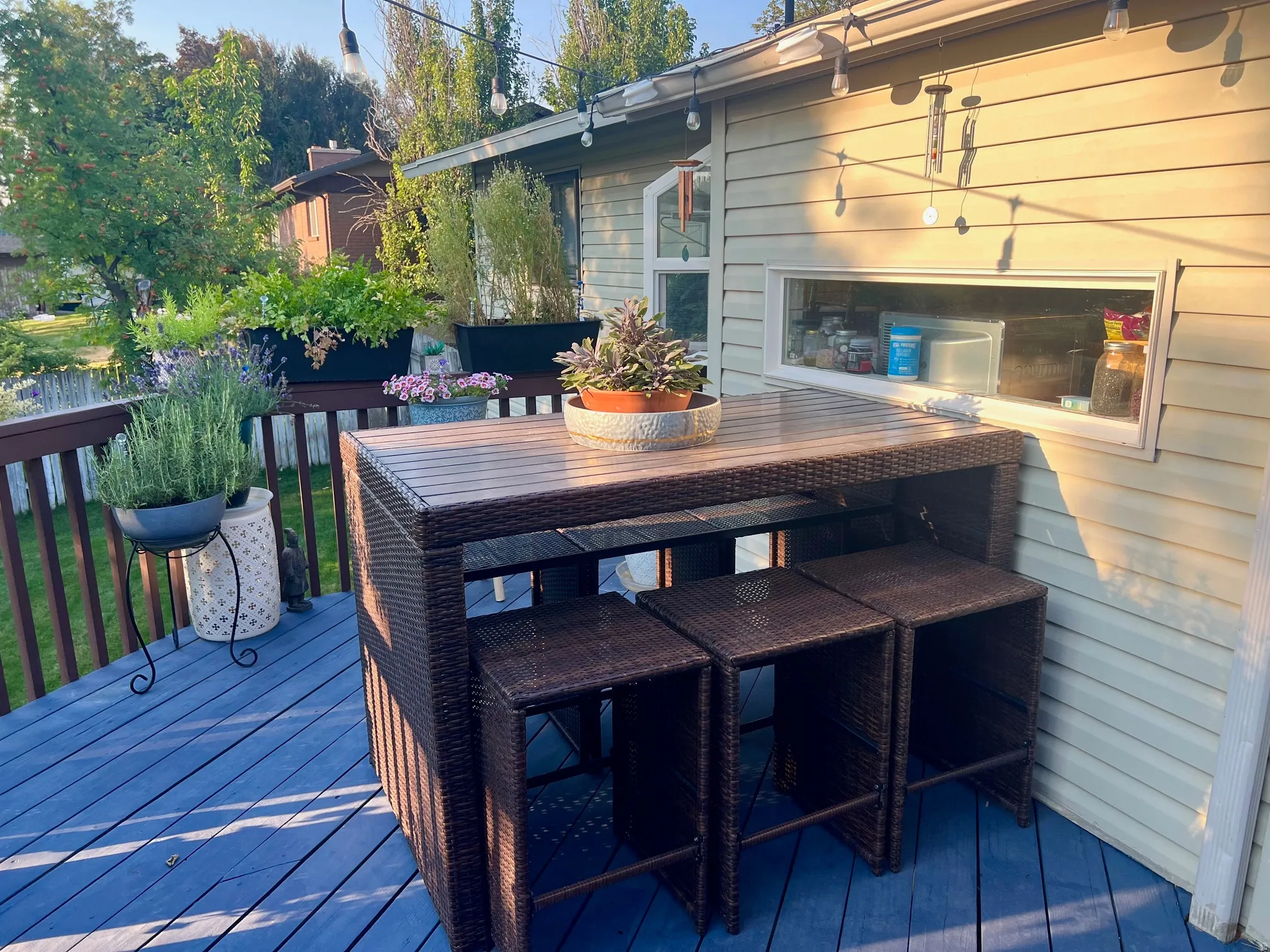 Expansive composite deck with integrated bar-height dining island featuring wood-finish countertop and open shelving storage, paired with matching woven rattan bar stools