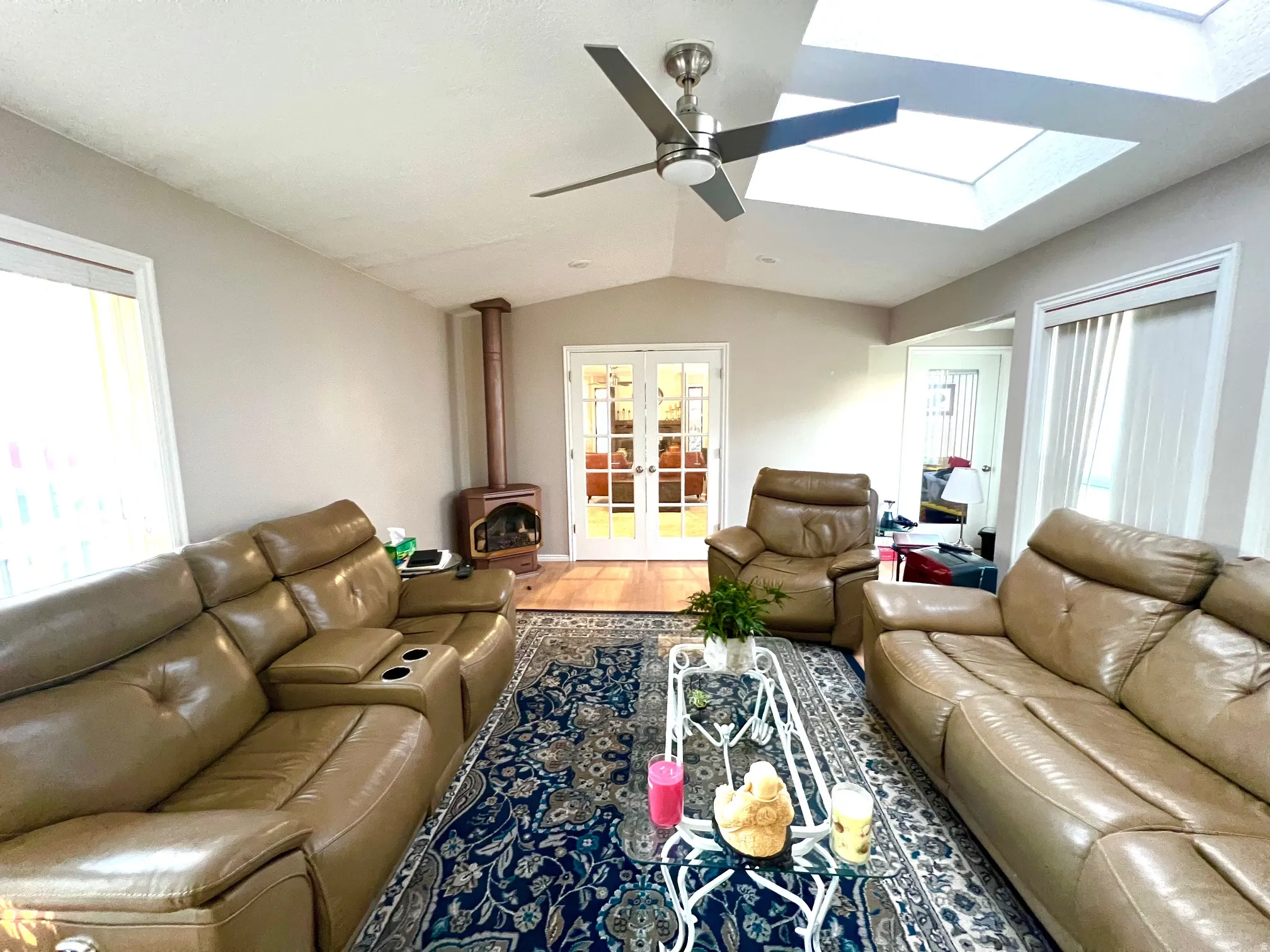 Vaulted ceiling with dual skylights, wood-burning stove, ceiling fan, and French doors