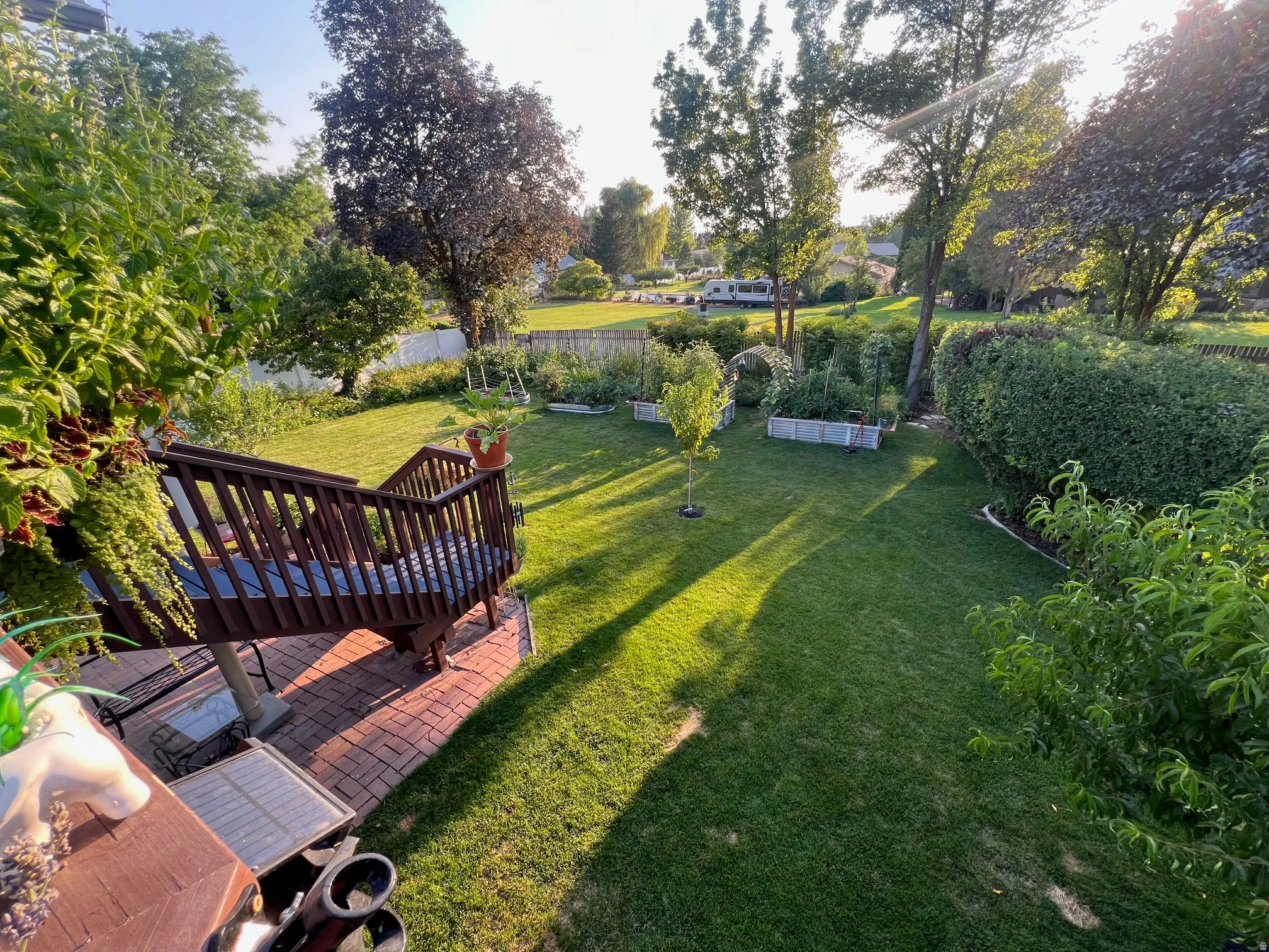 Expansive manicured lawn with mature specimen trees and lush hedging, anchored by a brick patio with wooden pergola structure