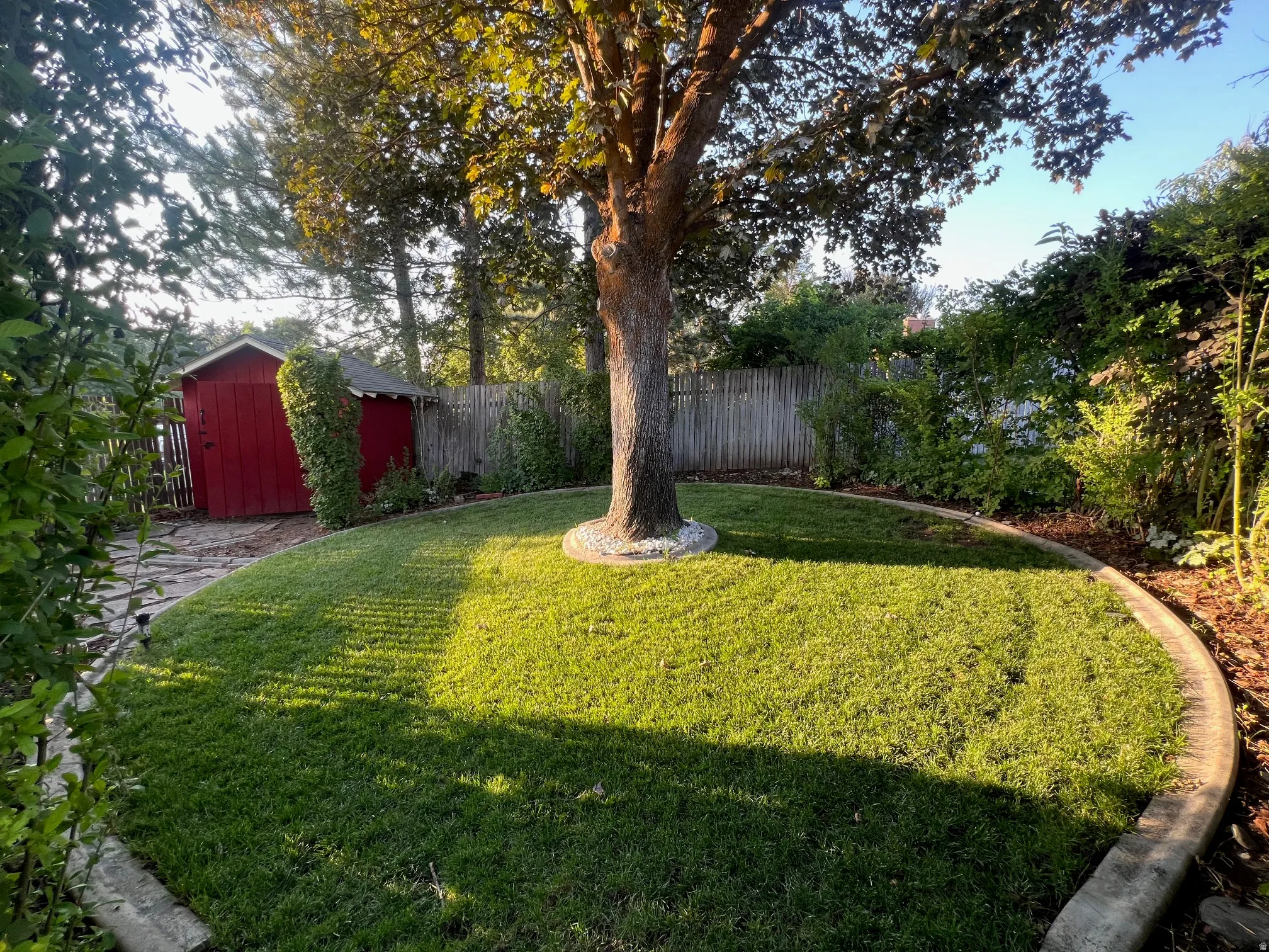 Mature shade tree anchors this expansive backyard oasis, featuring a lush, level lawn bordered by established landscaping and wooden fencing