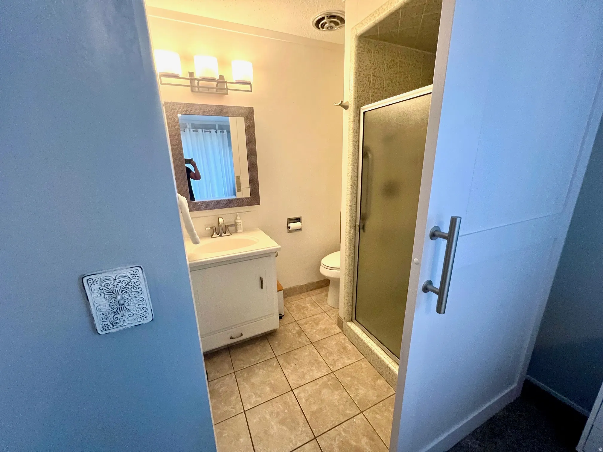 Tile flooring, white vanity with integrated sink, framed mirror, three-light vanity fixture, and a glass-enclosed shower