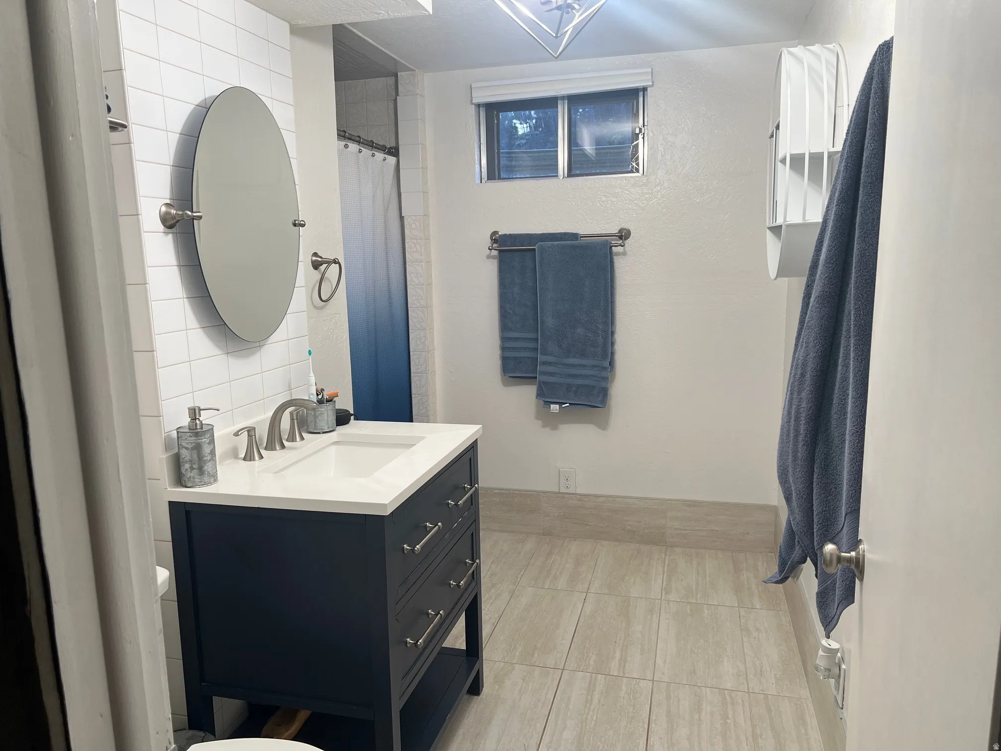 Spa-inspired primary bathroom featuring a dark vanity with multiple drawers, white quartz countertop, circular illuminated mirror, and polished chrome fixtures