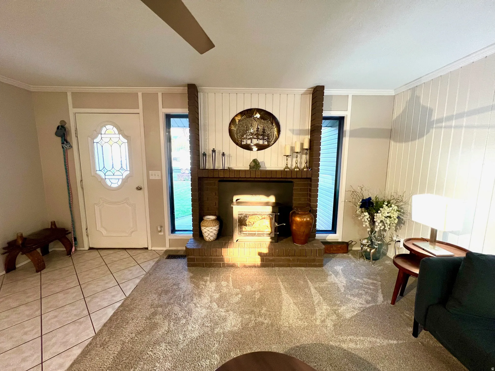Brick fireplace with a built-in stove, leaded glass entry door, ceiling fan, and tile flooring