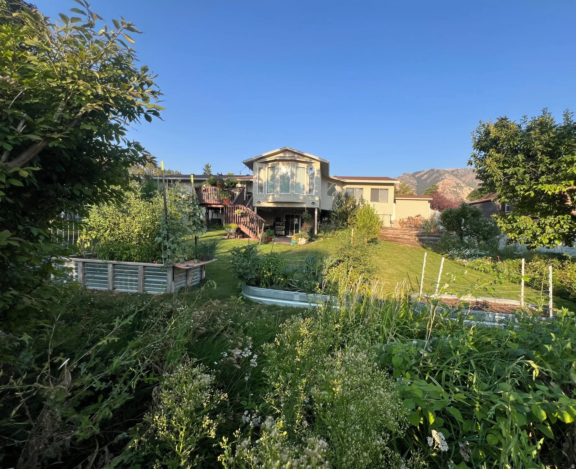 Expansive terraced backyard featuring multiple raised garden beds, a manicured lawn, and a multi-level deck with a bay window extension