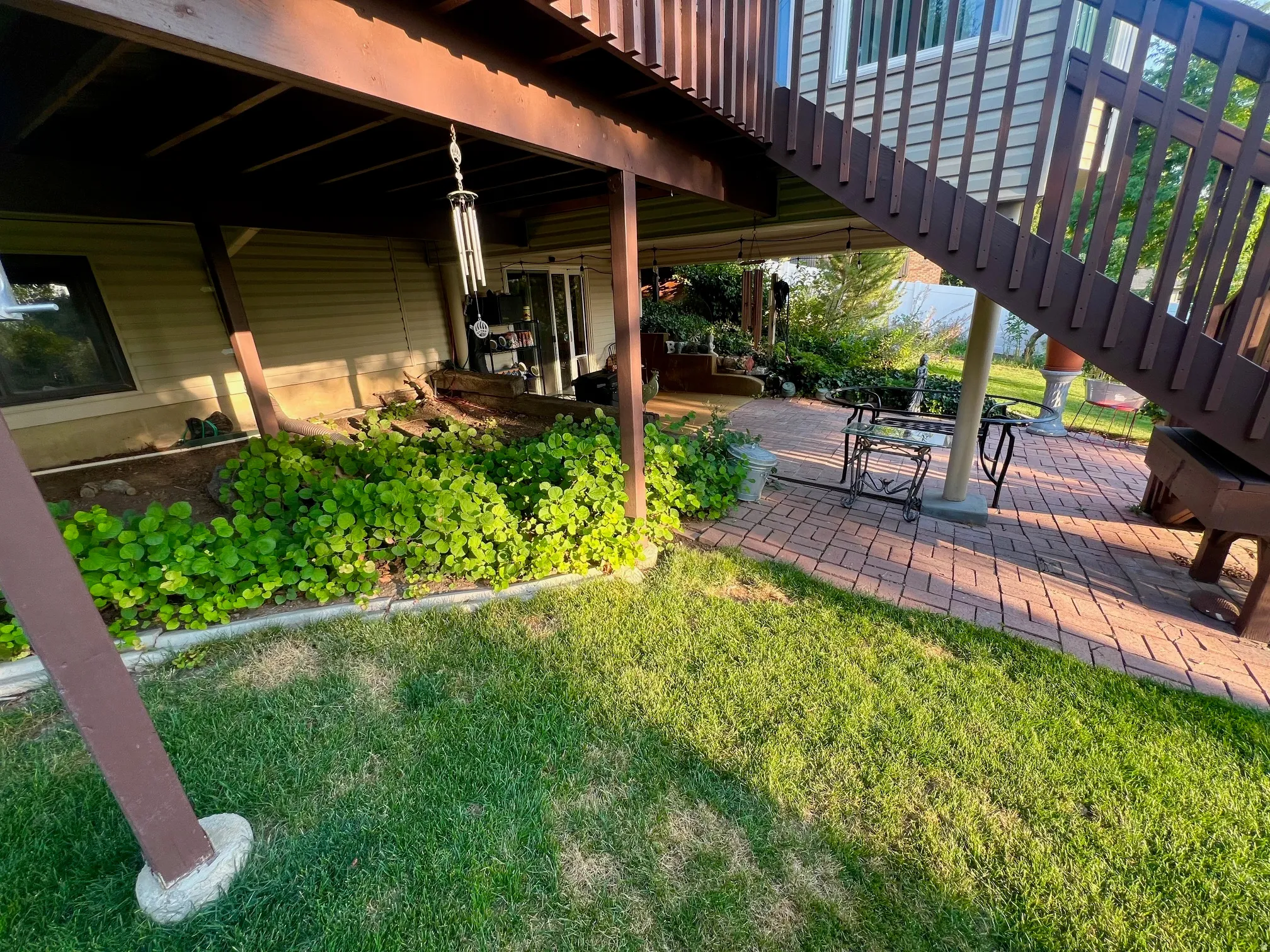 Covered patio with wooden beam construction overlooking a level lawn with mature landscaping, including lush shrub borders and established plantings