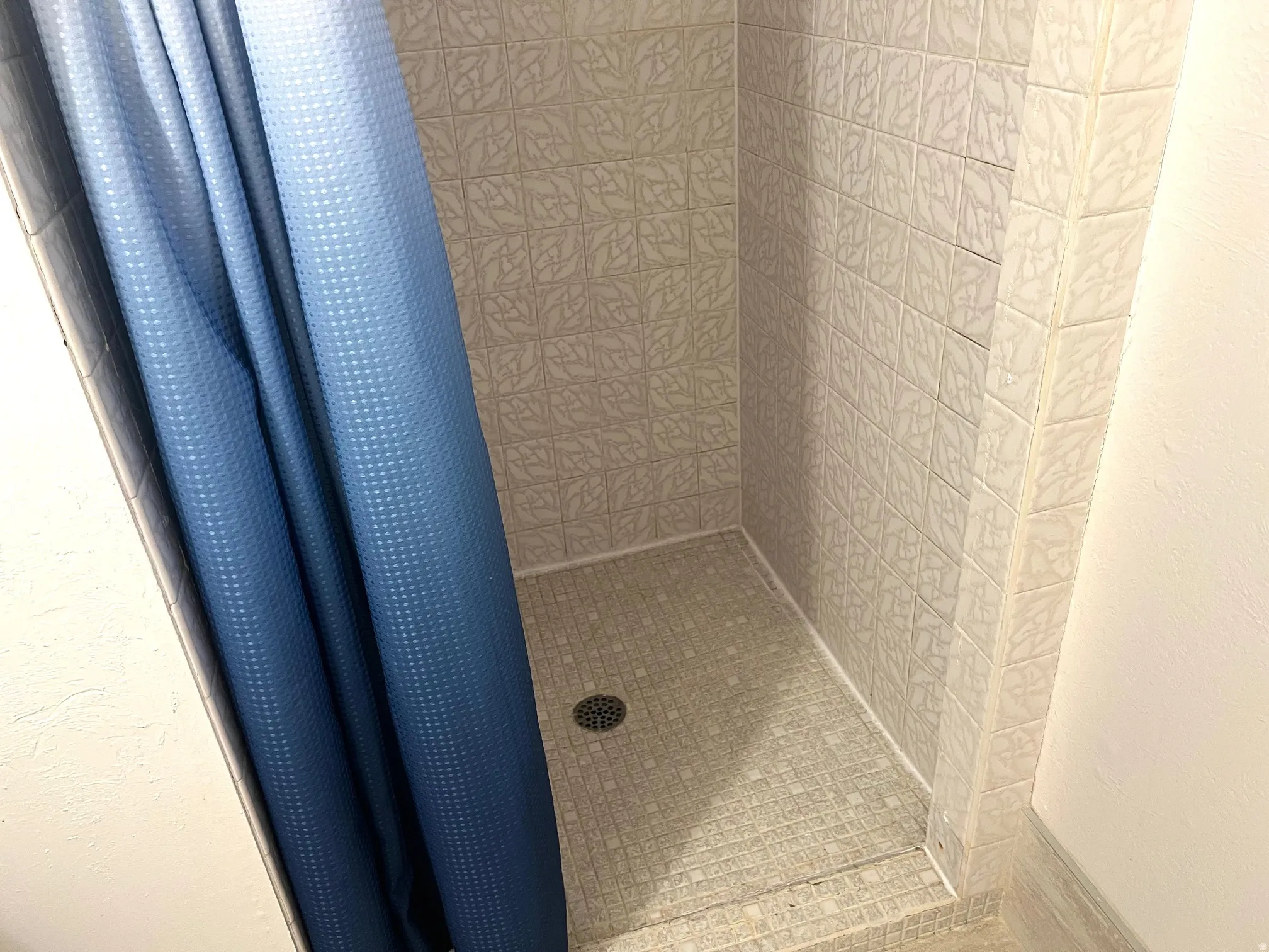 Shower stall featuring floor-to-ceiling square tiles with an embossed pattern and a mosaic tile base