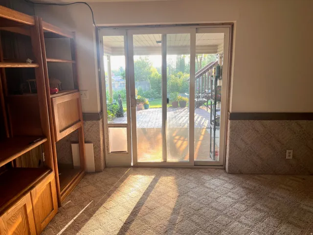 Built-in wood-finish shelving with cabinetry, patterned carpet flooring, and a sliding glass door