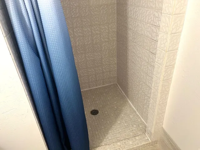Shower stall featuring floor-to-ceiling square tiles with an embossed pattern and a mosaic tile base
