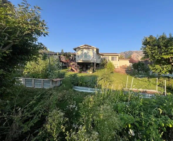 Expansive terraced backyard featuring multiple raised garden beds, a manicured lawn, and a multi-level deck with a bay window extension