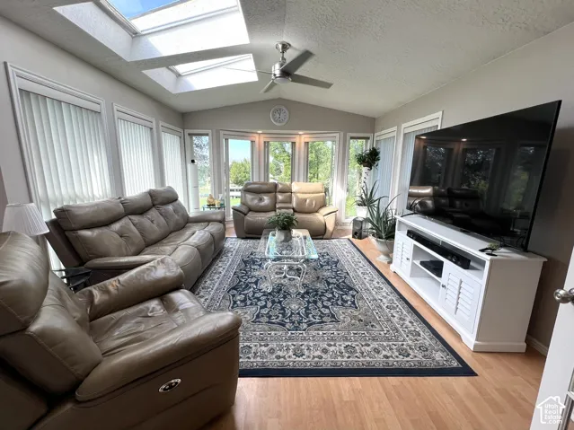 Vaulted ceiling with multiple skylights, ceiling fan, wood-finish flooring, and extensive window-line