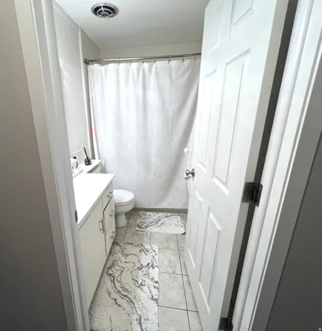 White paneled door, light-colored tile flooring, white vanity with cabinet storage, white shower curtain, and a ceiling-mounted exhaust fan