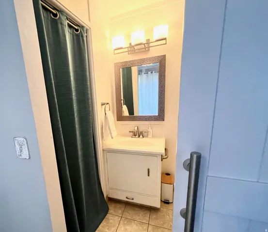Vanity with integrated sink, framed mirror, wall-mounted light fixture, and tile flooring