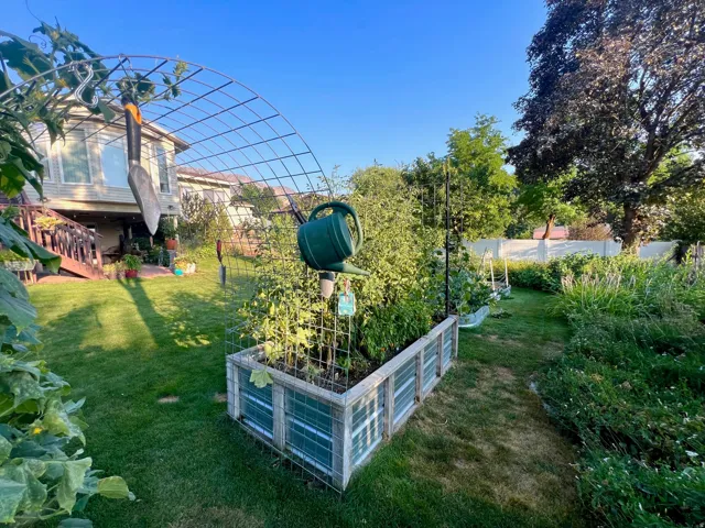 Expansive backyard featuring a manicured lawn, raised garden beds, established perimeter foliage, and a multi-level deck with wood railings