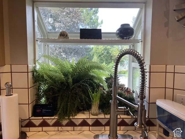 White framed window with a lower shelf, a pre-rinse style faucet, and white square tile backsplash with a decorative border
