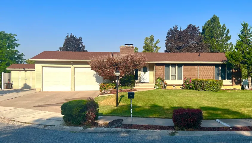 Ranch-style exterior with a two-car garage, front lawn, and mature landscaping