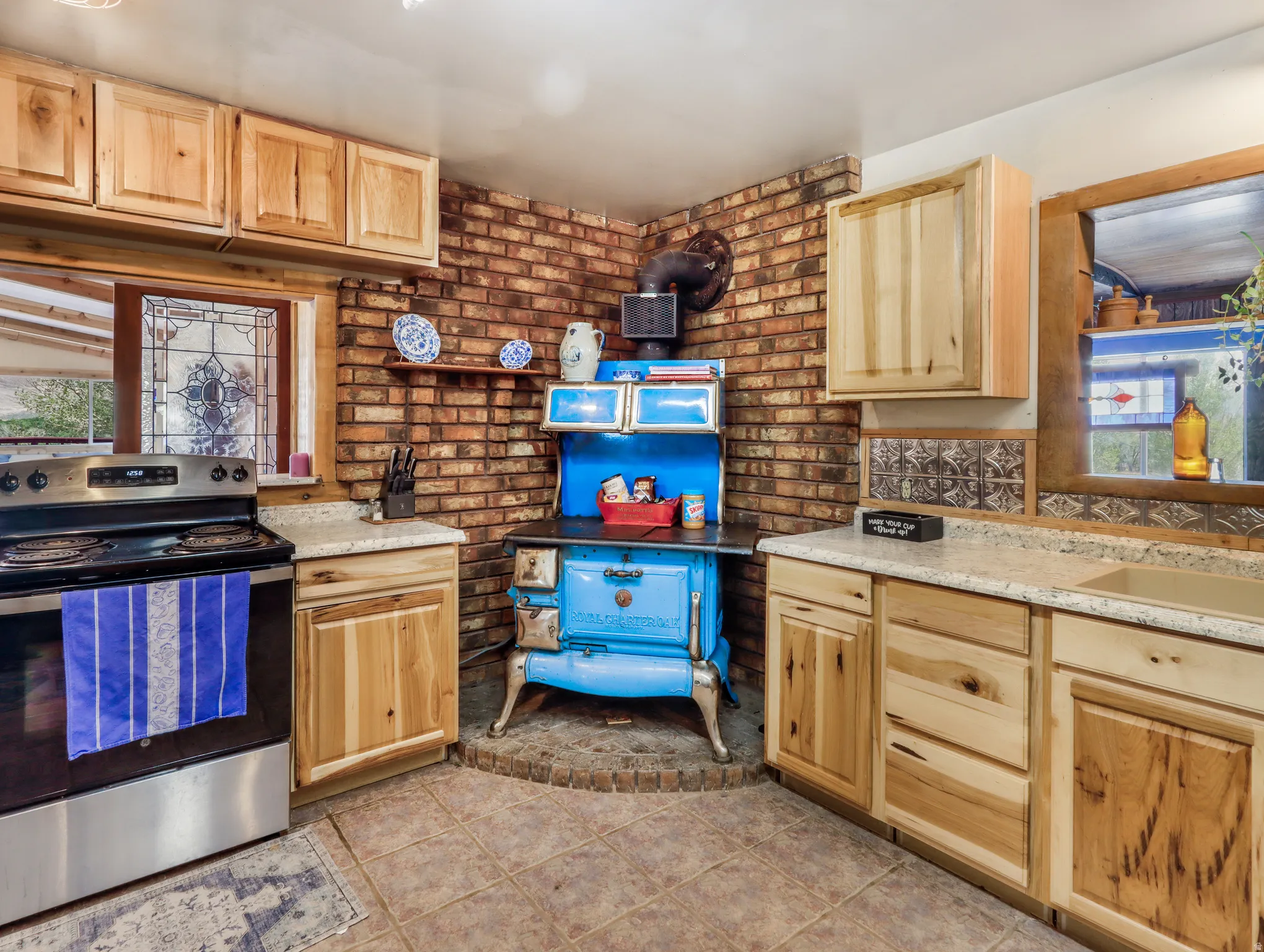 Kitchen featuring light wood cabinetry, light-toned countertops, a stainless steel electric range, and a brick accent wall
