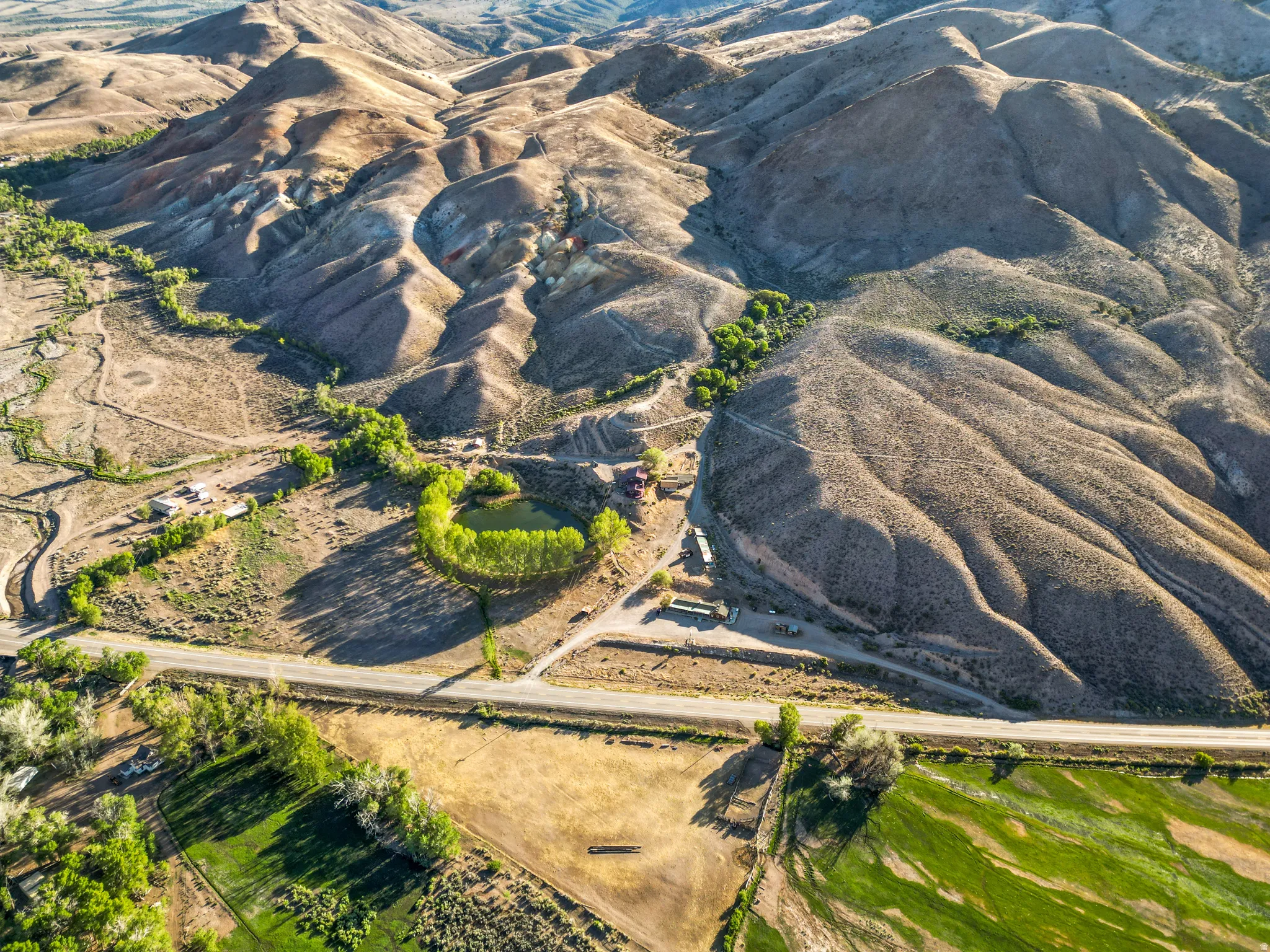 Expansive natural landscape featuring rolling hills, a meandering waterway, a prominent pond, a paved roadway, and green agricultural land