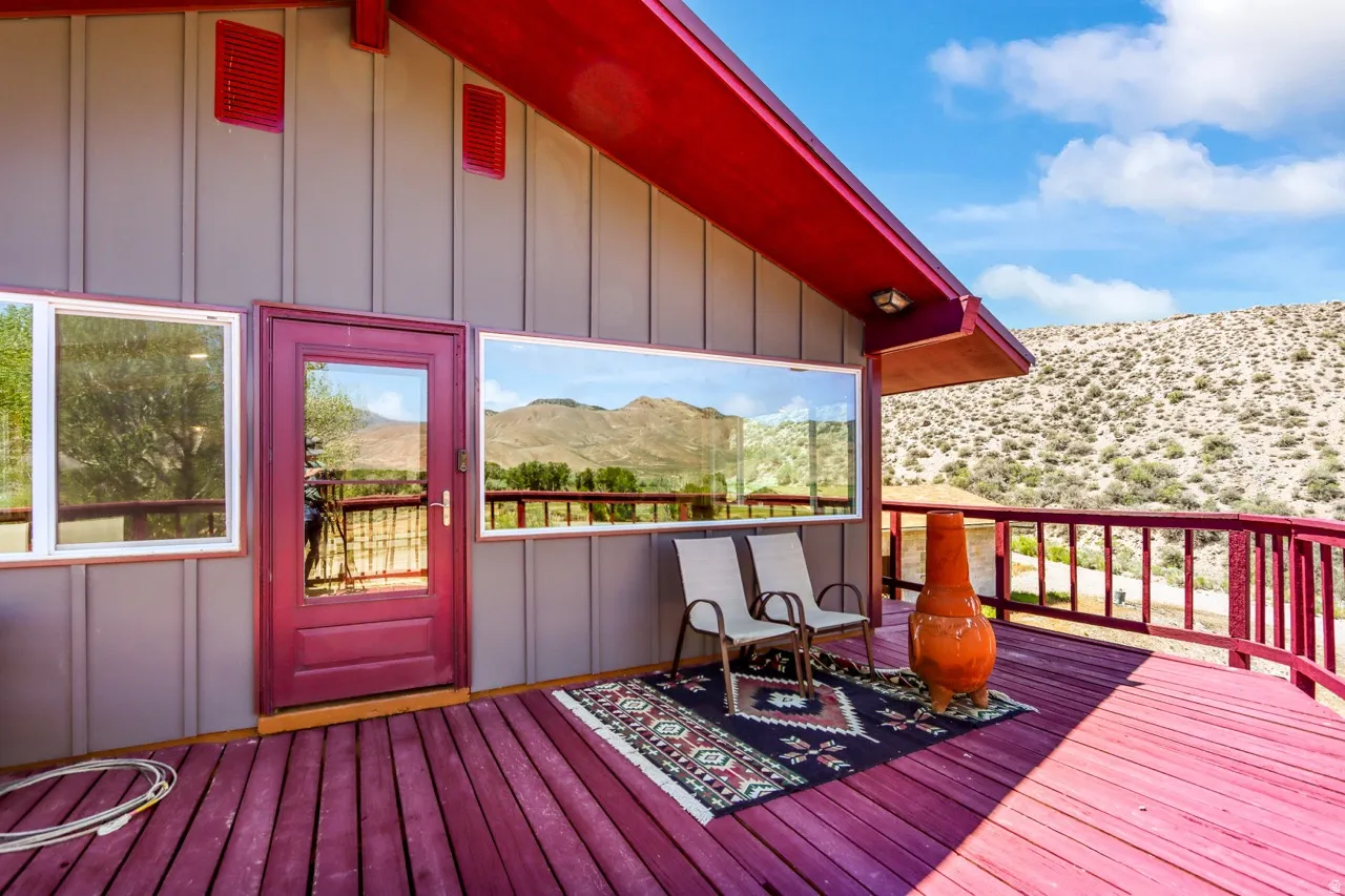 Expansive outdoor deck with red-painted railings and flooring, featuring a glass-paned entry door and large windows