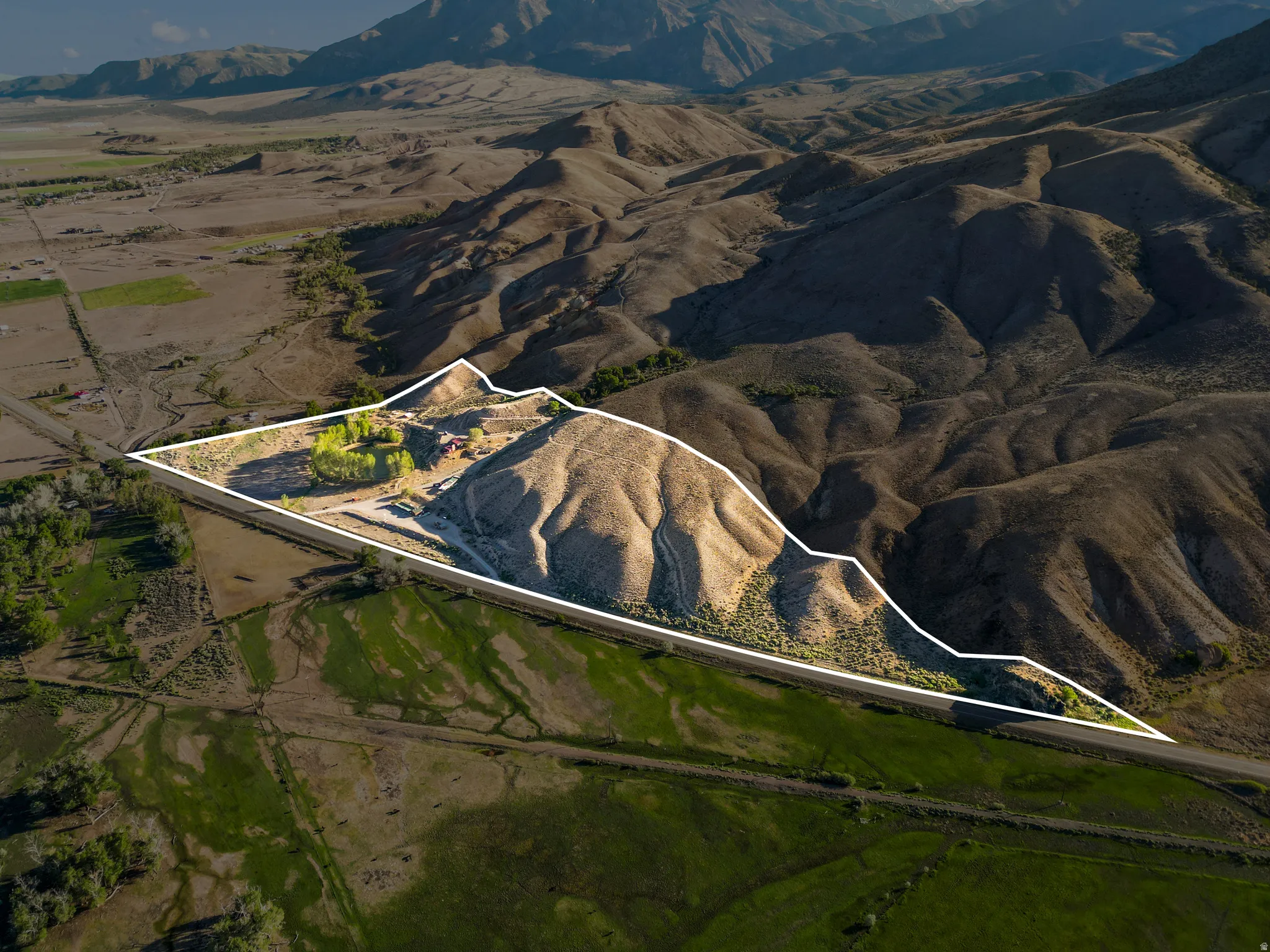 Expansive property featuring varied terrain, a defined parcel boundary, direct road access, and mountainous backdrops