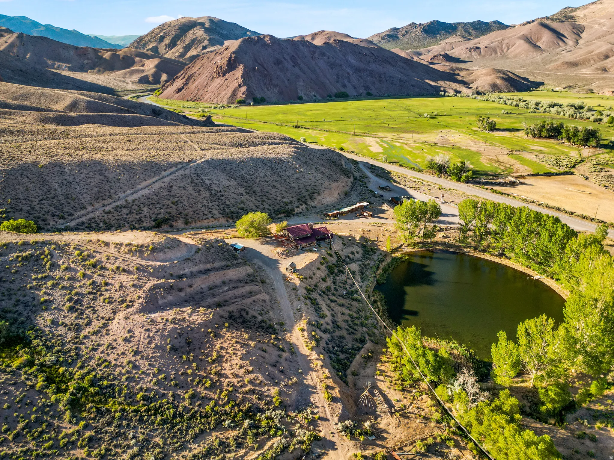 Hillside property with a natural pond, surrounding mature trees, and a paved road access