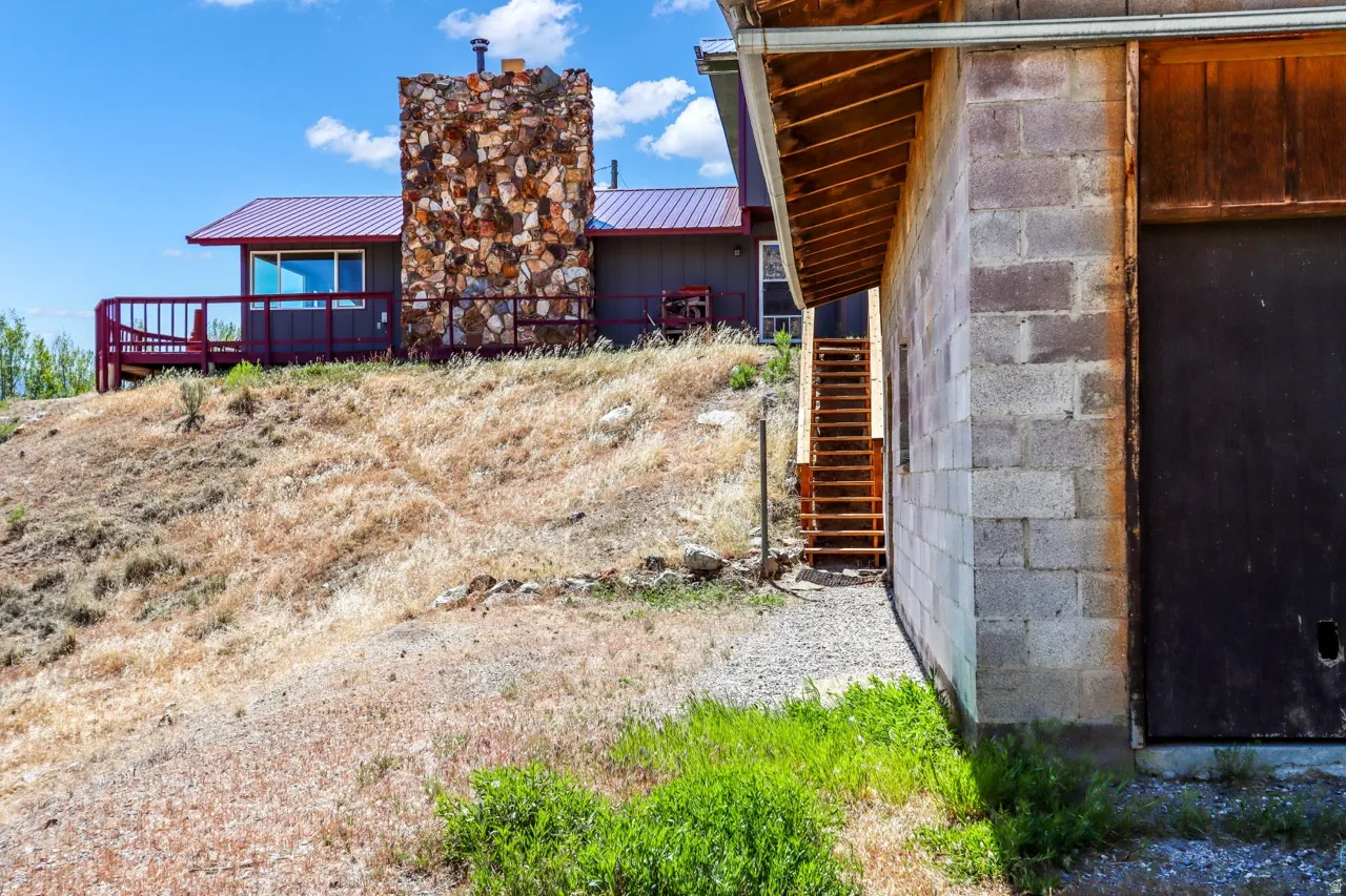 Stone-clad chimney, red metal roof, expansive deck with red railing, and a concrete block structure