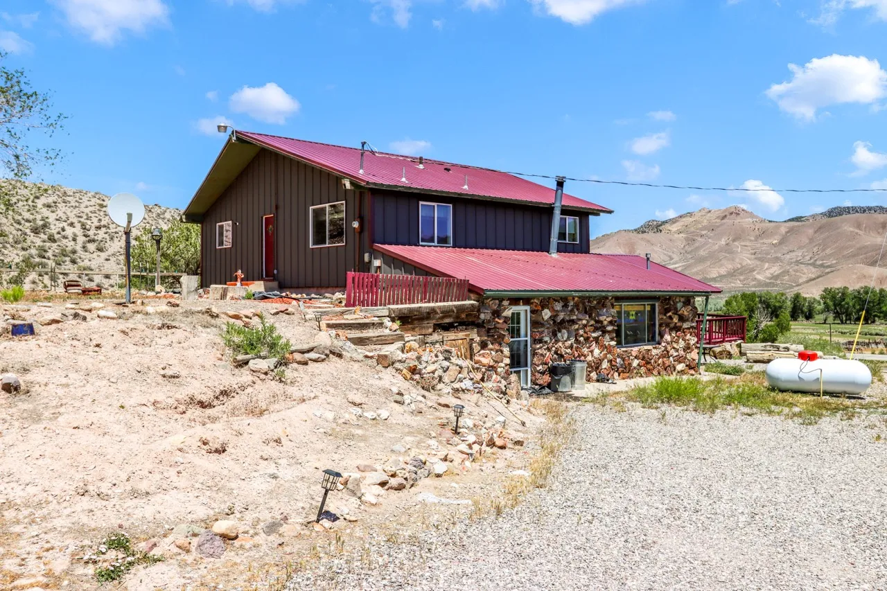 Red metal roofing, brown board-and-batten siding, stone facade, and a gravel driveway