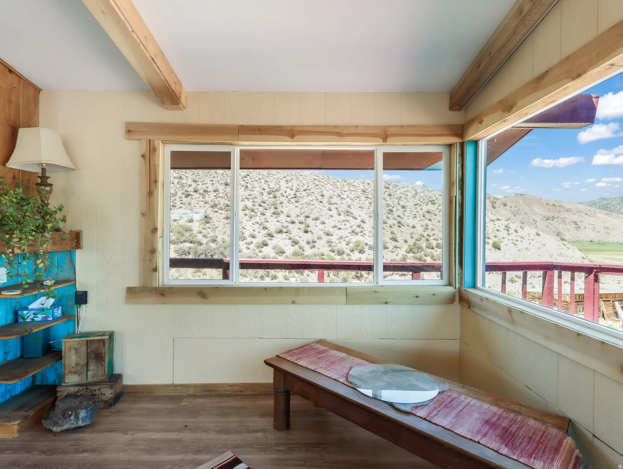 Exposed wood beams, wood-finish flooring, wood trim around windows, built-in shelving unit, and an expansive window with a desert landscape